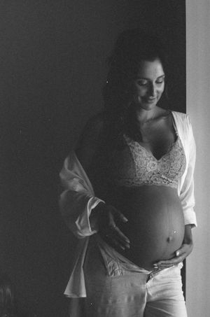 Black and white photo of a smiling pregnant woman in a lace bra and open robe, cradling her baby bump.