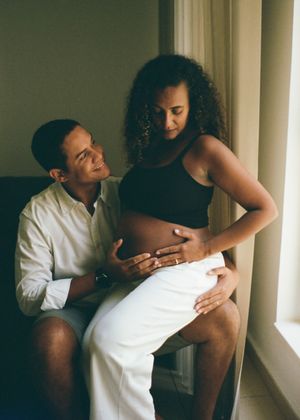 Couple sharing a tender maternity moment by a window, man smiling at pregnant woman cradling her baby bump.