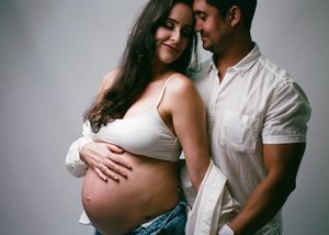 Couple sharing a tender moment during maternity photo shoot, pregnant woman cradling baby bump.