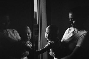 Black and white photo of a parent holding a baby near a window with reflections visible in the glass.
