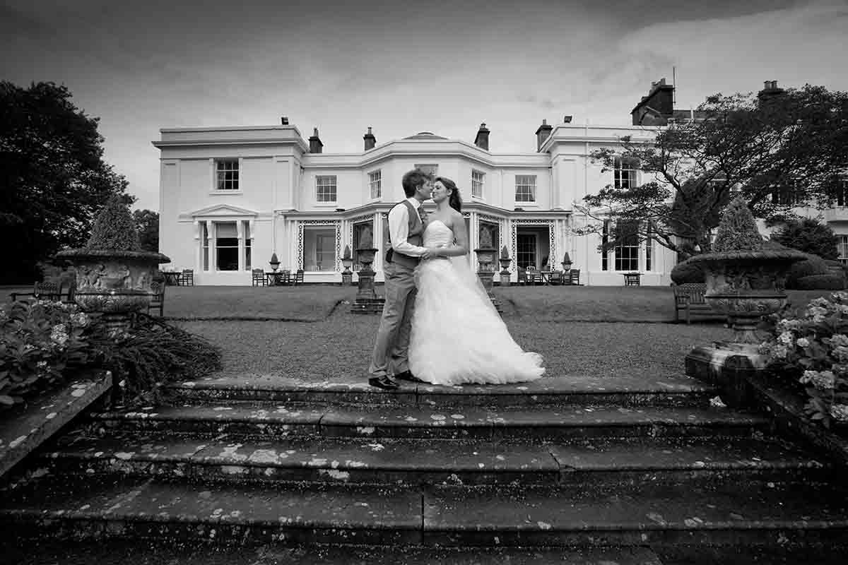 Couple stand in front of Storrs Hall in Windermere for their wedding photographs