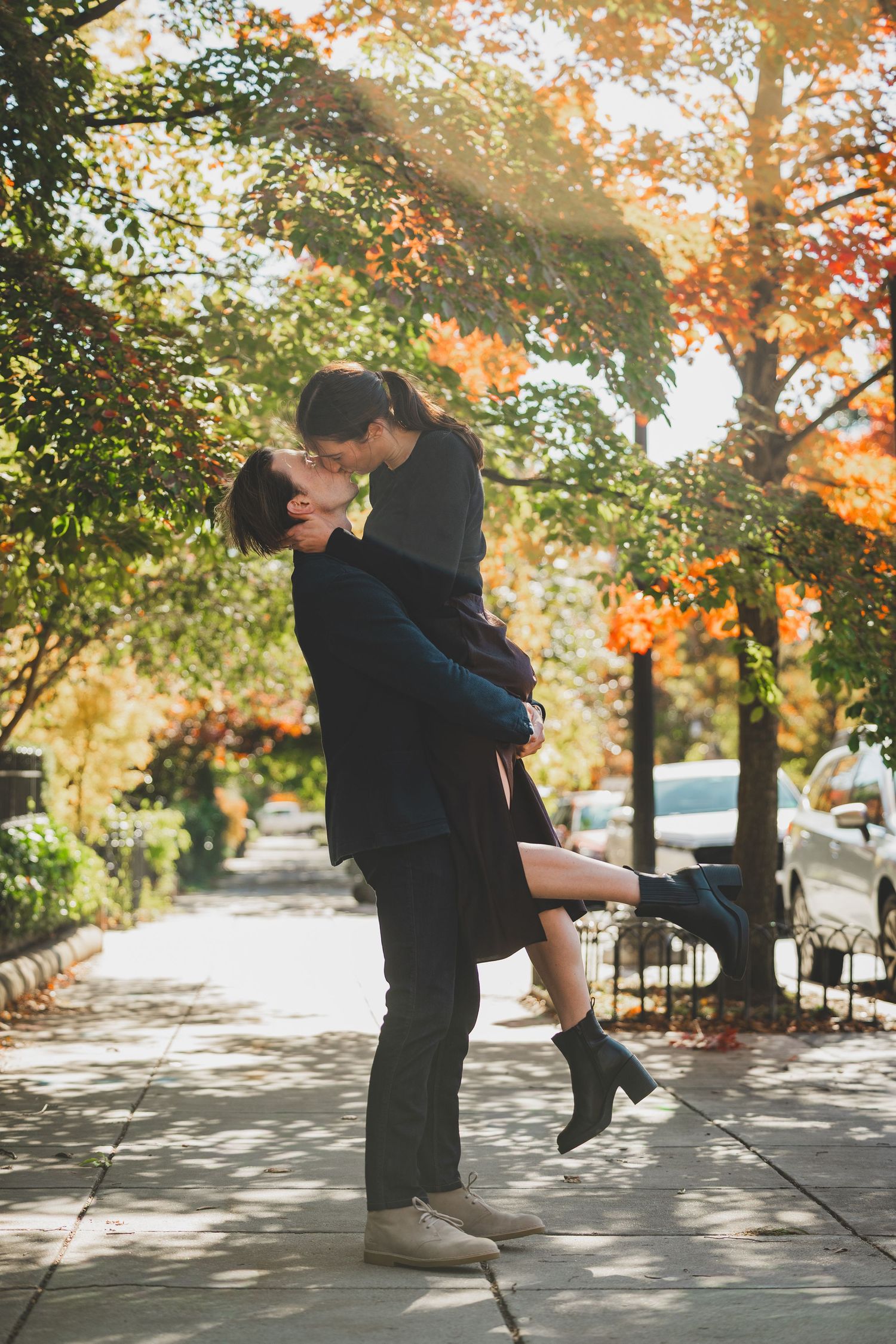 Couple sharing a romantic kiss outdoors in autumn, man lifting woman with colorful fall foliage at Lincoln Memorial Park