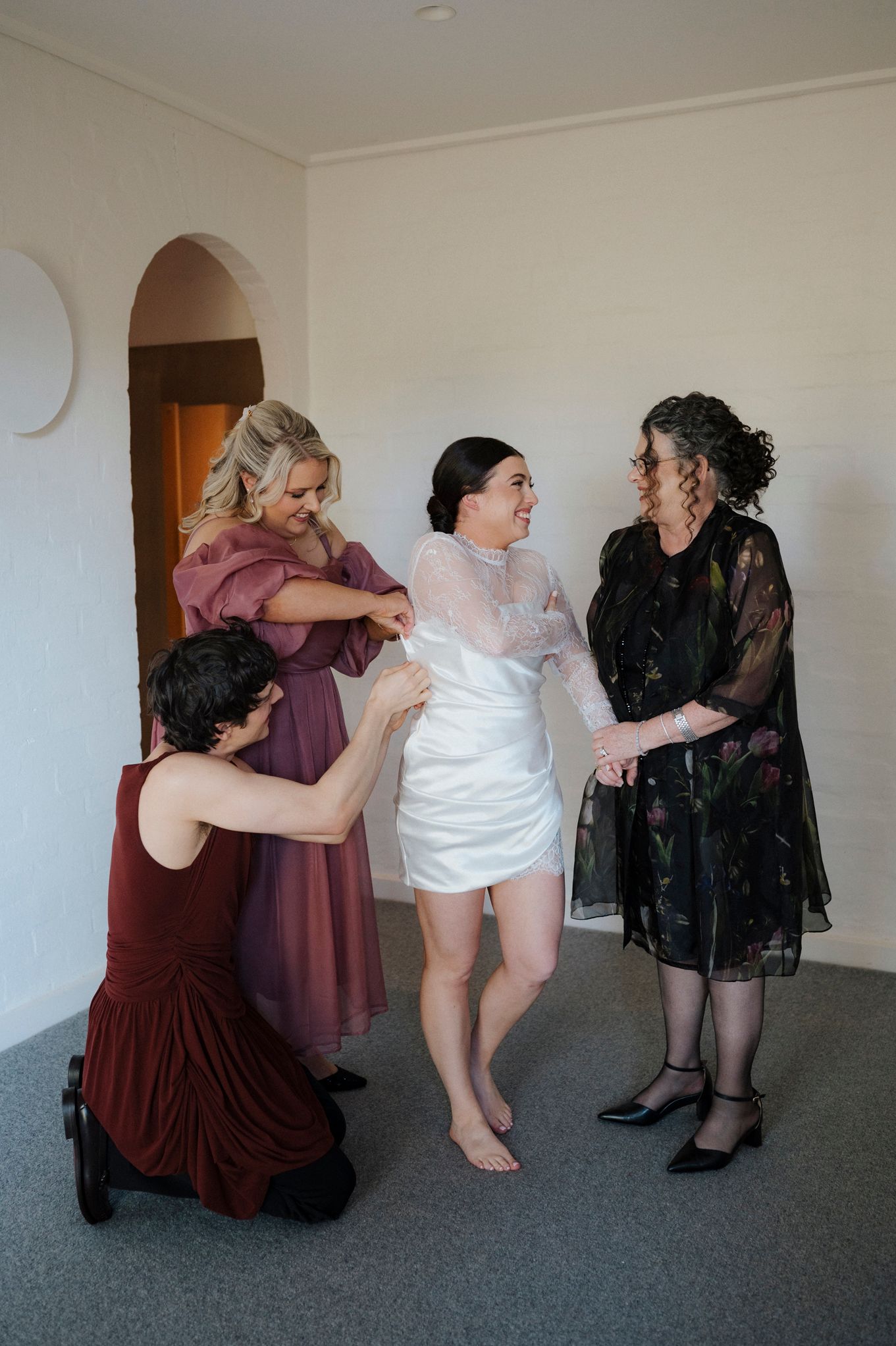 Bride being helped into her wedding dress by bridesmaids and family member in a bright room.