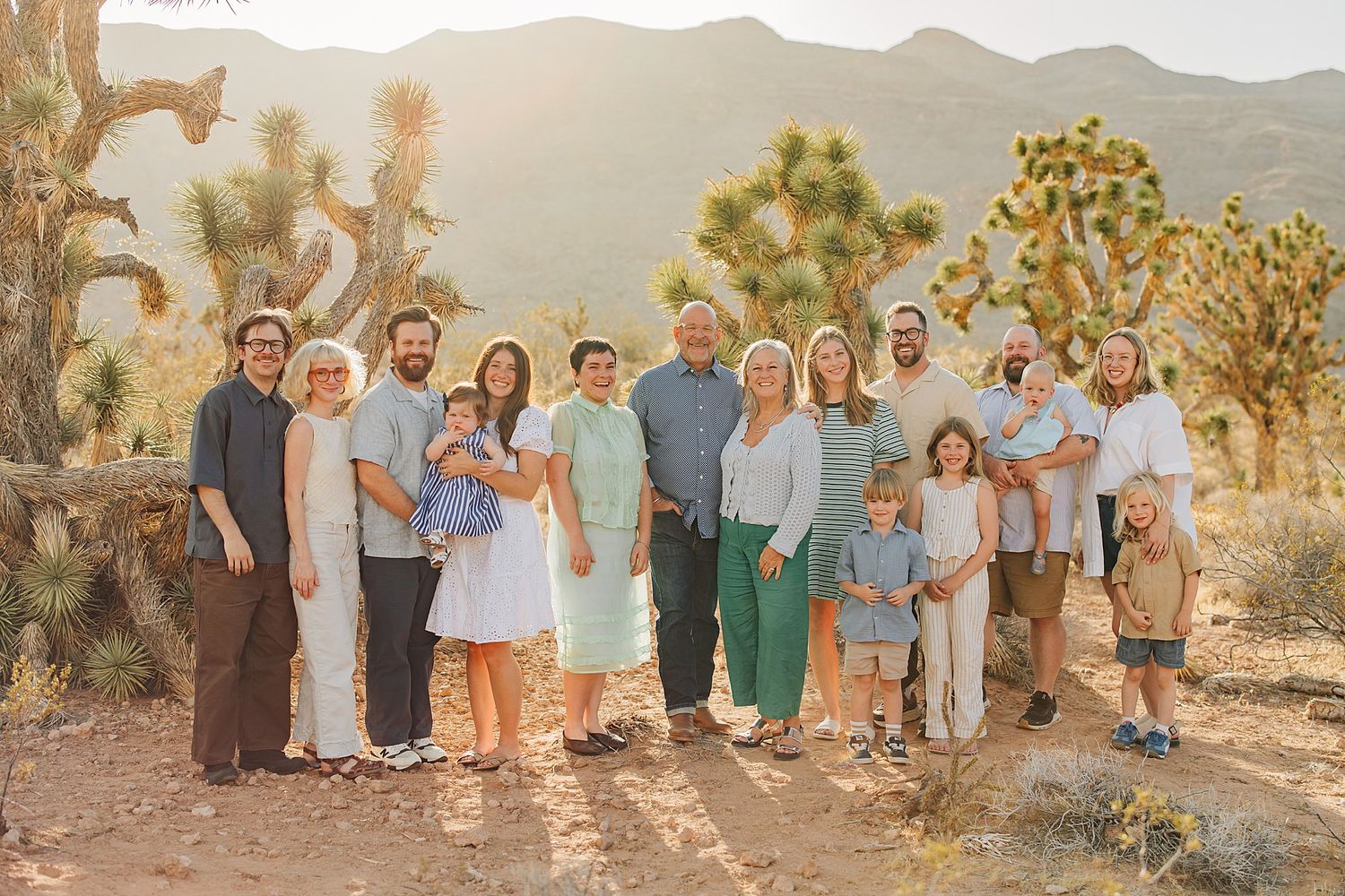 Large family portrait outdoors in Joshua Tree desert landscape at golden hour, mountains in background.