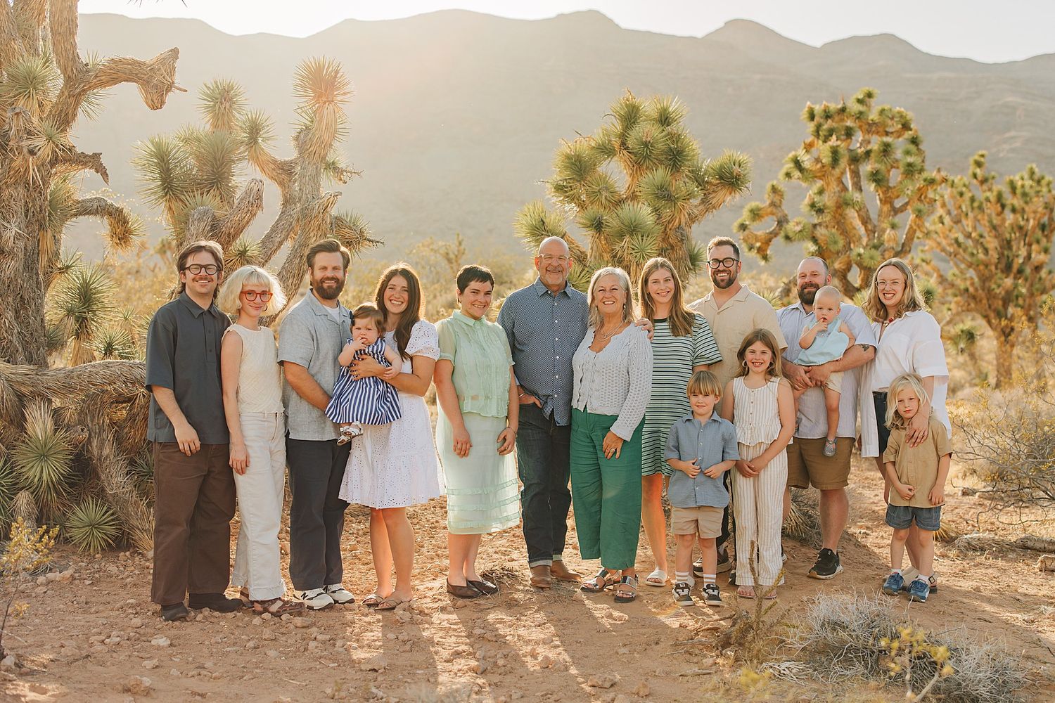 Large family group portrait outdoors in Joshua Tree desert landscape at golden hour with mountains in background.