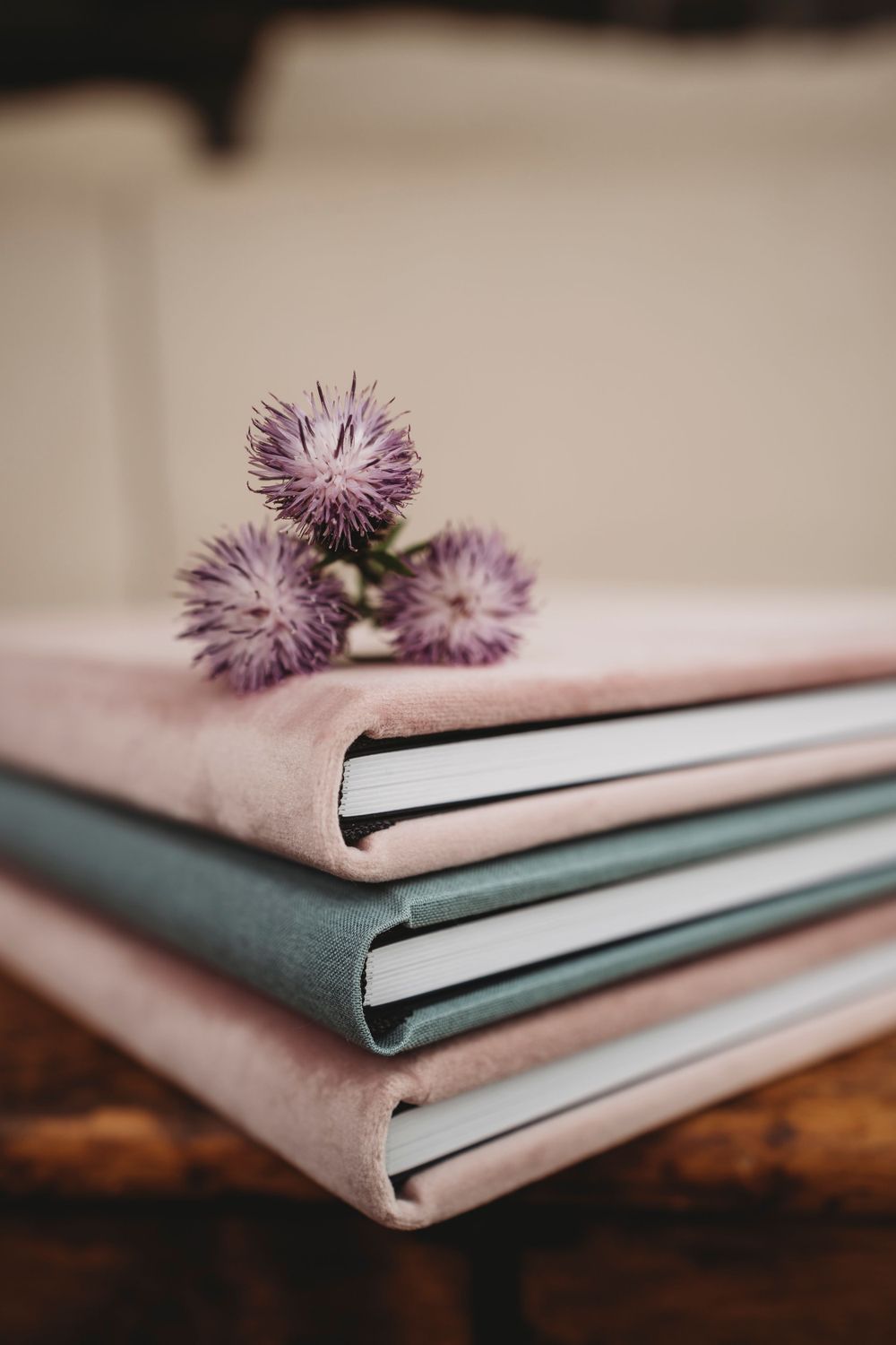 Stack of soft pink and sage green notebooks with purple thistle flowers on top.
