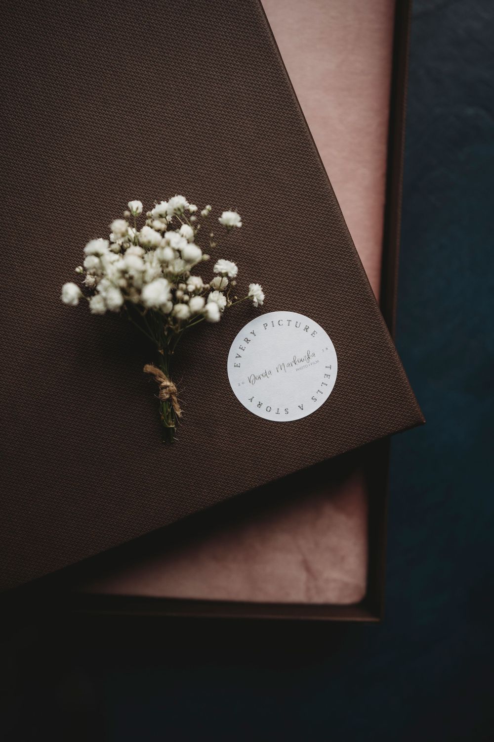 A brown photo album with baby's breath flower and a round label.