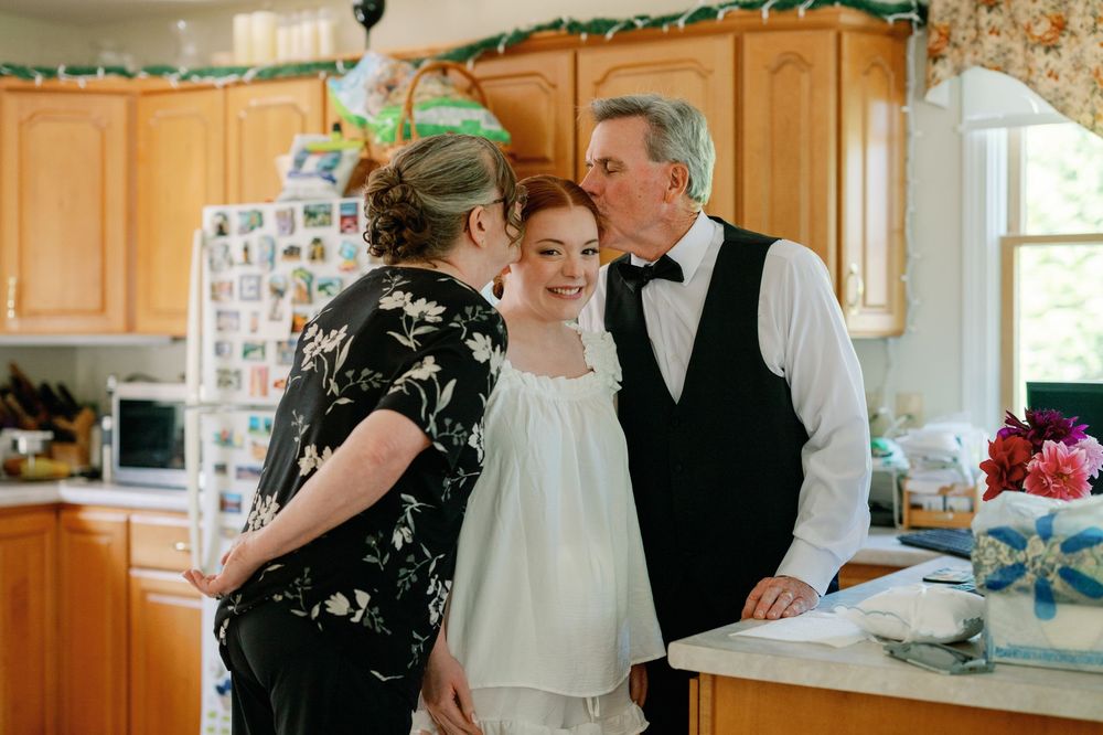 Elderly couple sharing a tender moment with a young woman in a home kitchen during a special occasion.