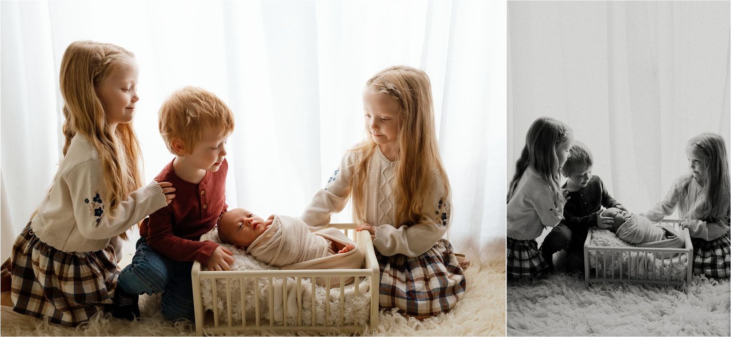 Two young sisters lovingly interact with their baby sibling in a cozy studio setting with soft natural light.