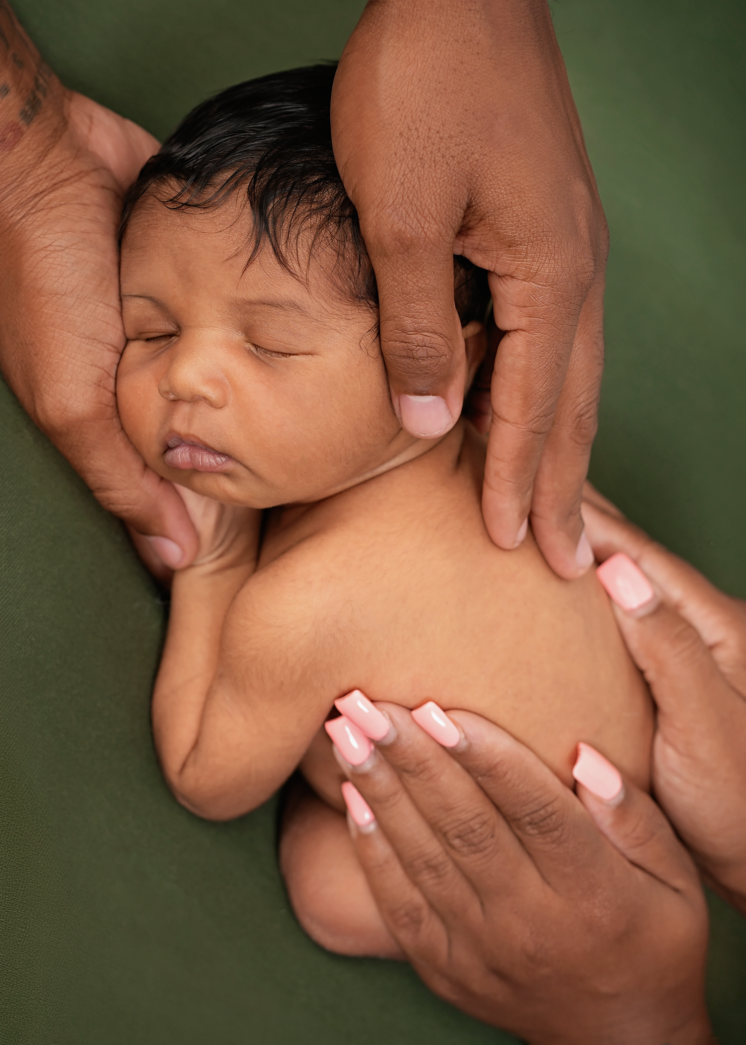 Newborn baby Travis gently supported by his parents' hands during his newborn photography session.