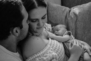 Black and white photo of new parents tenderly gazing at their newborn baby while relaxing on a couch.