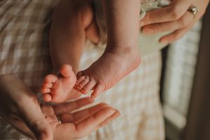A parent gently holds a newborn baby's tiny feet in their cupped hands, showcasing delicate infant toes.