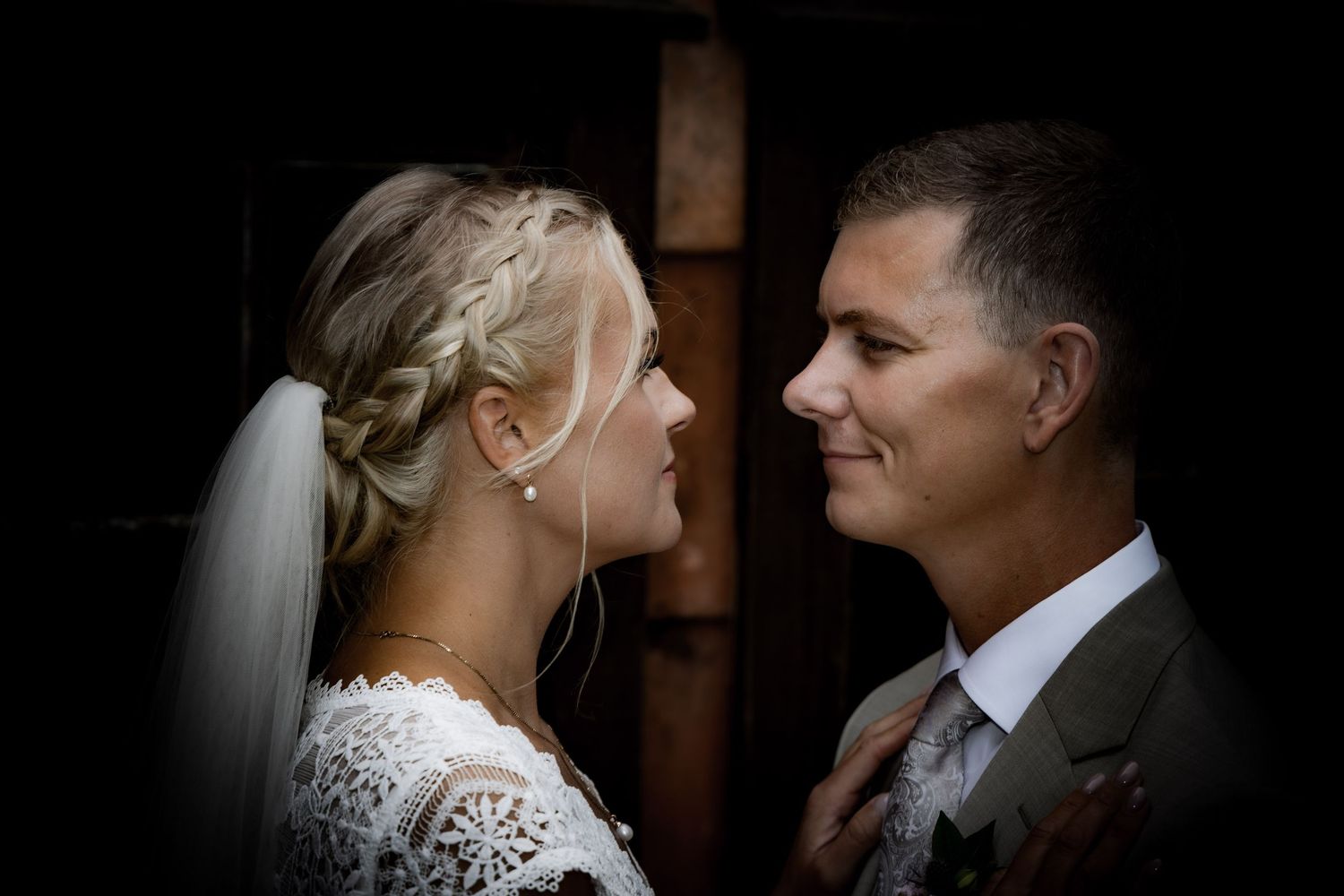 Bride and groom share an intimate moment, facing each other closely, bride wearing lace dress and veil.