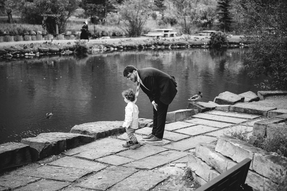 Black and white photo of a man bending down to a small child on stone steps beside a calm reflective lake.