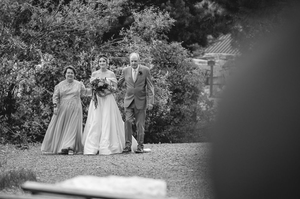 Black and white photo of a bride walking with her parents down a garden path on her wedding day.
