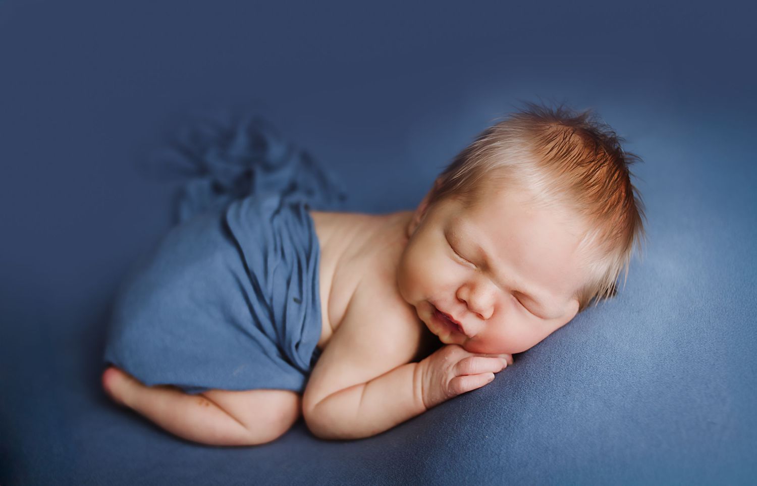 Peaceful newborn baby sleeping wrapped in a soft blue blanket on a blue background in a professional photo.