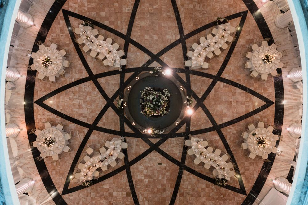 Ornate ceiling with geometric star pattern, mosaic tiles, and chandelier lights viewed from below.