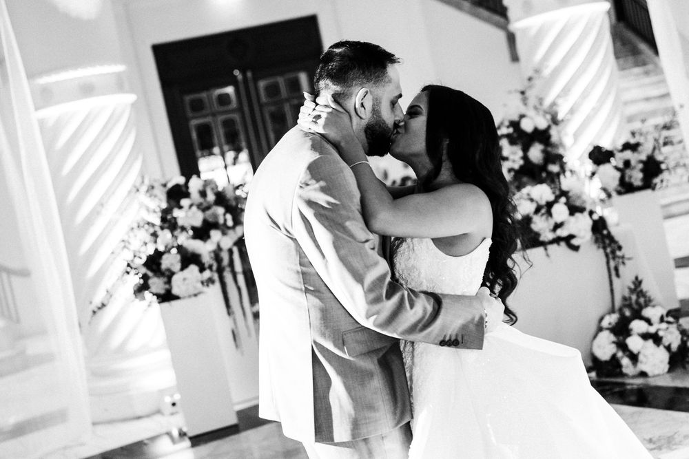 Black and white photo of a bride and groom sharing a romantic first kiss at their elegant wedding ceremony.