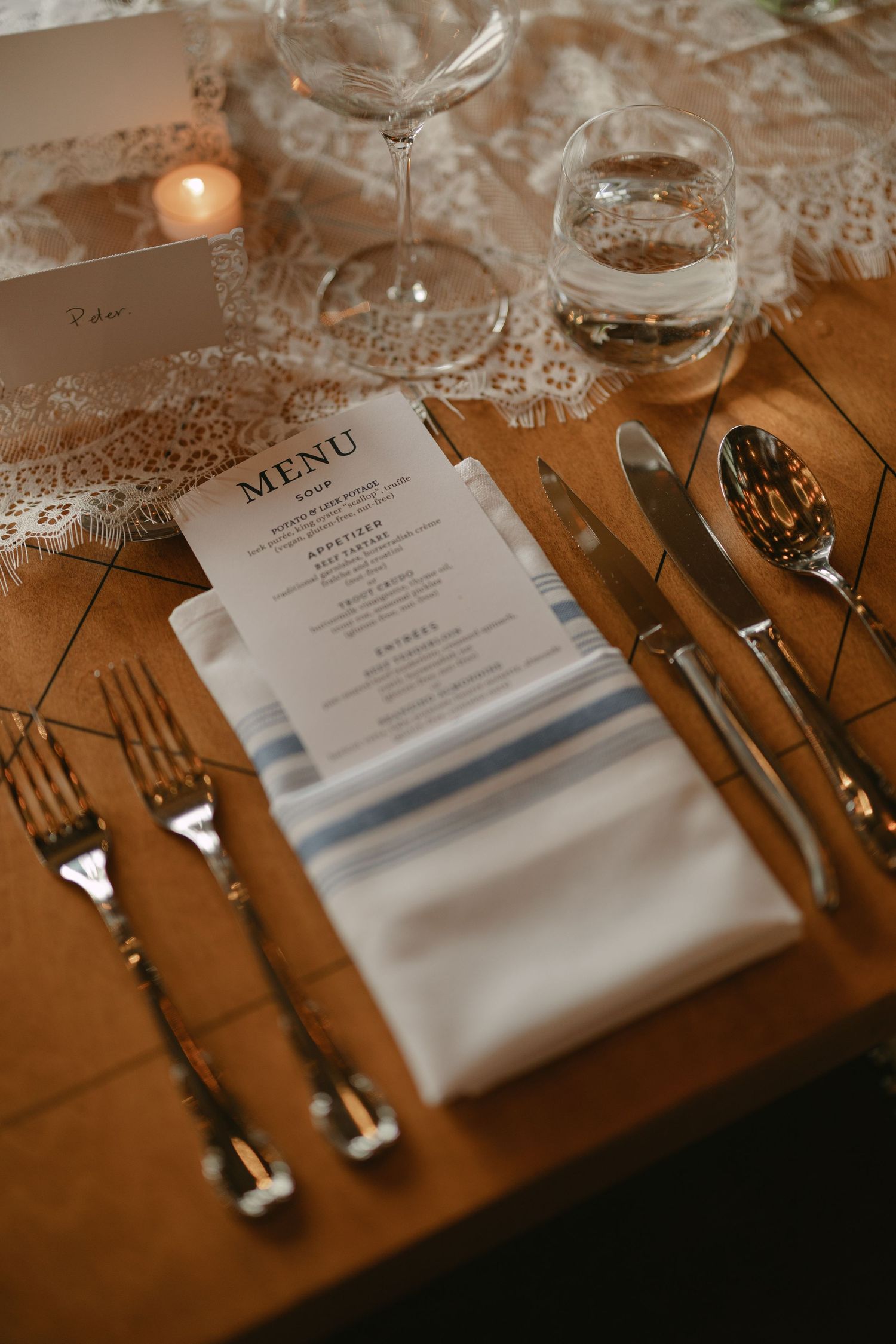 Elegant wedding place setting with striped linen napkin, printed menu card, silver cutlery, and crystal glasses.