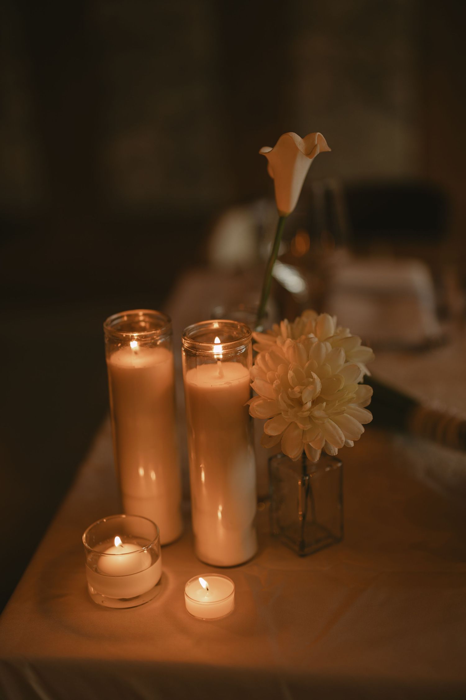 Elegant wedding centerpiece with tall white pillar candles, tea lights, and white flowers on draped table.