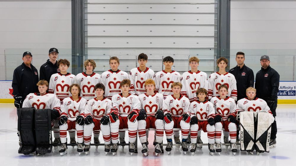 Youth hockey team poses for official group photo in white and red uniforms on indoor ice rink.