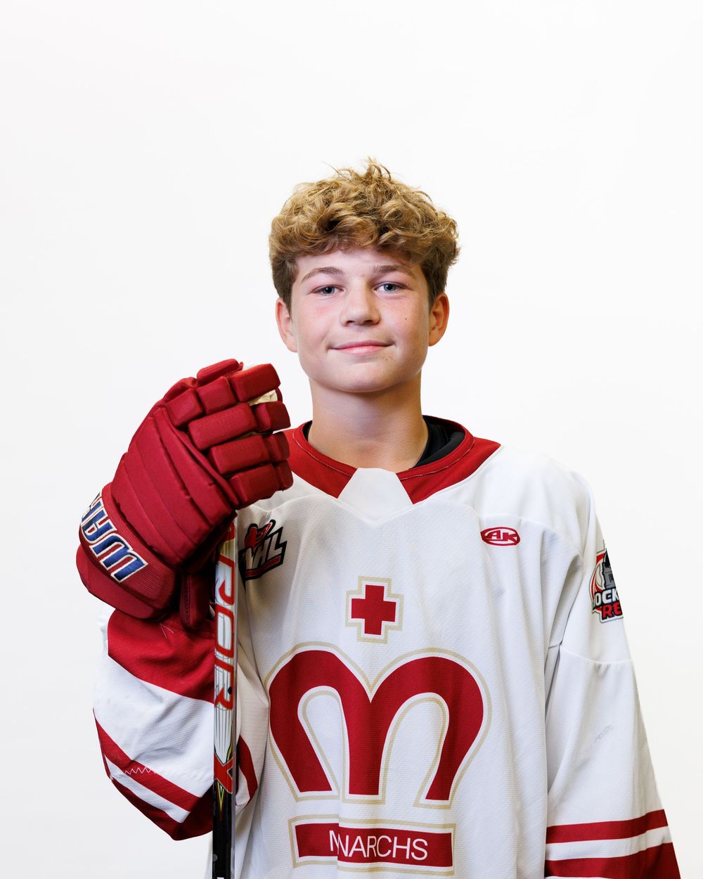 Young hockey player in white Monarchs jersey holding red glove up for team portrait photo.