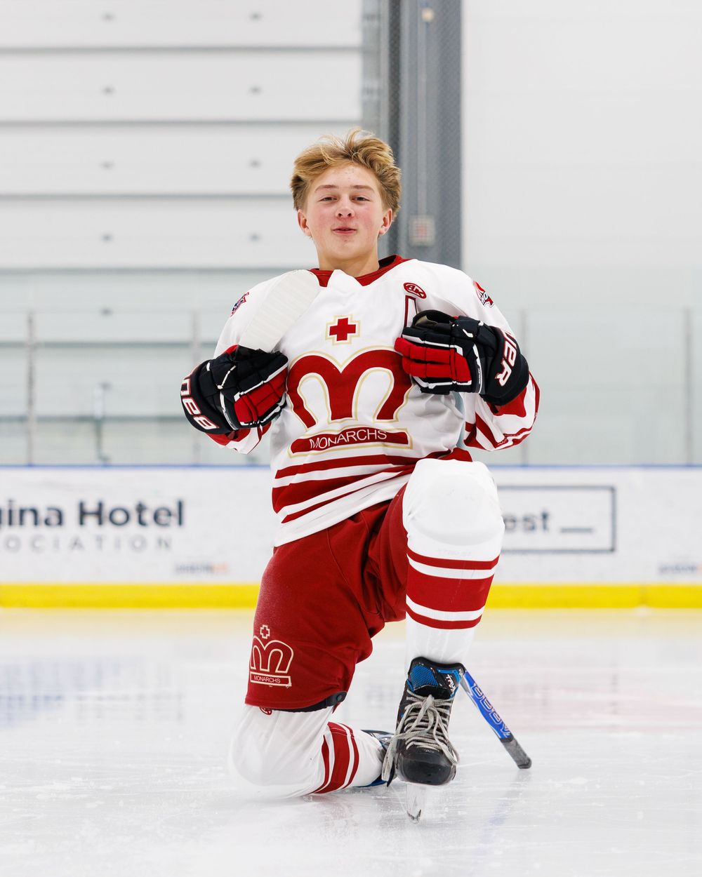 Young hockey player in red and white jersey kneeling on ice rink during game.