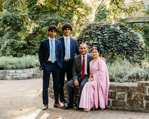 Family of four posing in a lush garden, dressed in formal attire including a pink sari and blue suits.