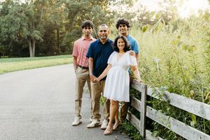 Family of four posing on a scenic path by a wooden fence, surrounded by lush greenery in warm golden light.