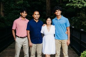 Family of four posing on a wooden bridge surrounded by lush green trees in an outdoor setting.