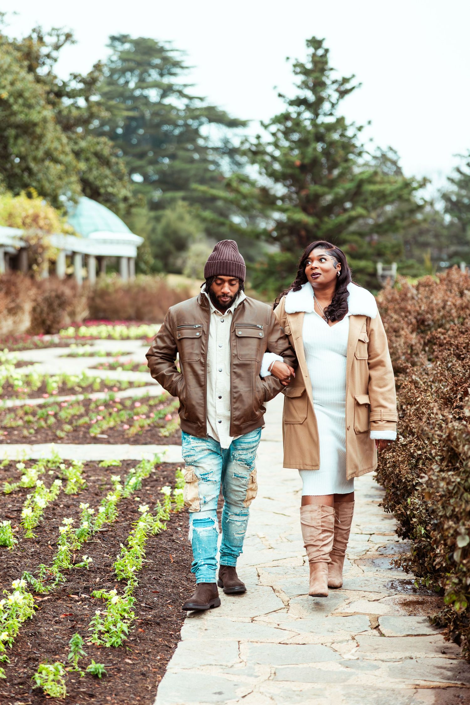 Couple walks hand-in-hand along garden path surrounded by lush greenery in autumn.