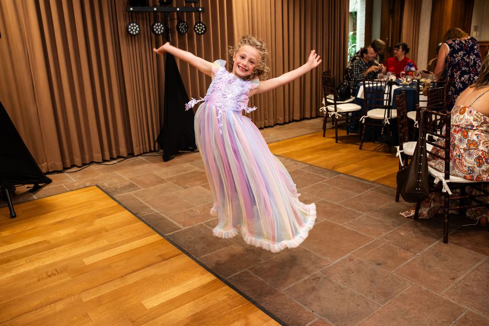 Young girl in purple tulle dress twirling joyfully on dance floor at elegant wedding reception.