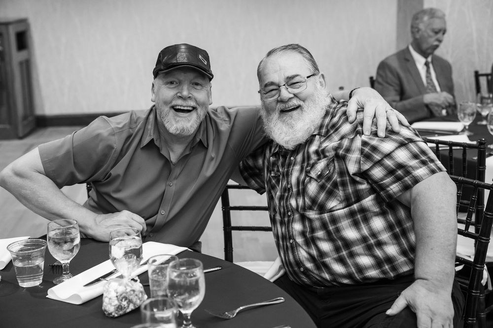 Two bearded men smile together at a banquet table in a black and white photo.