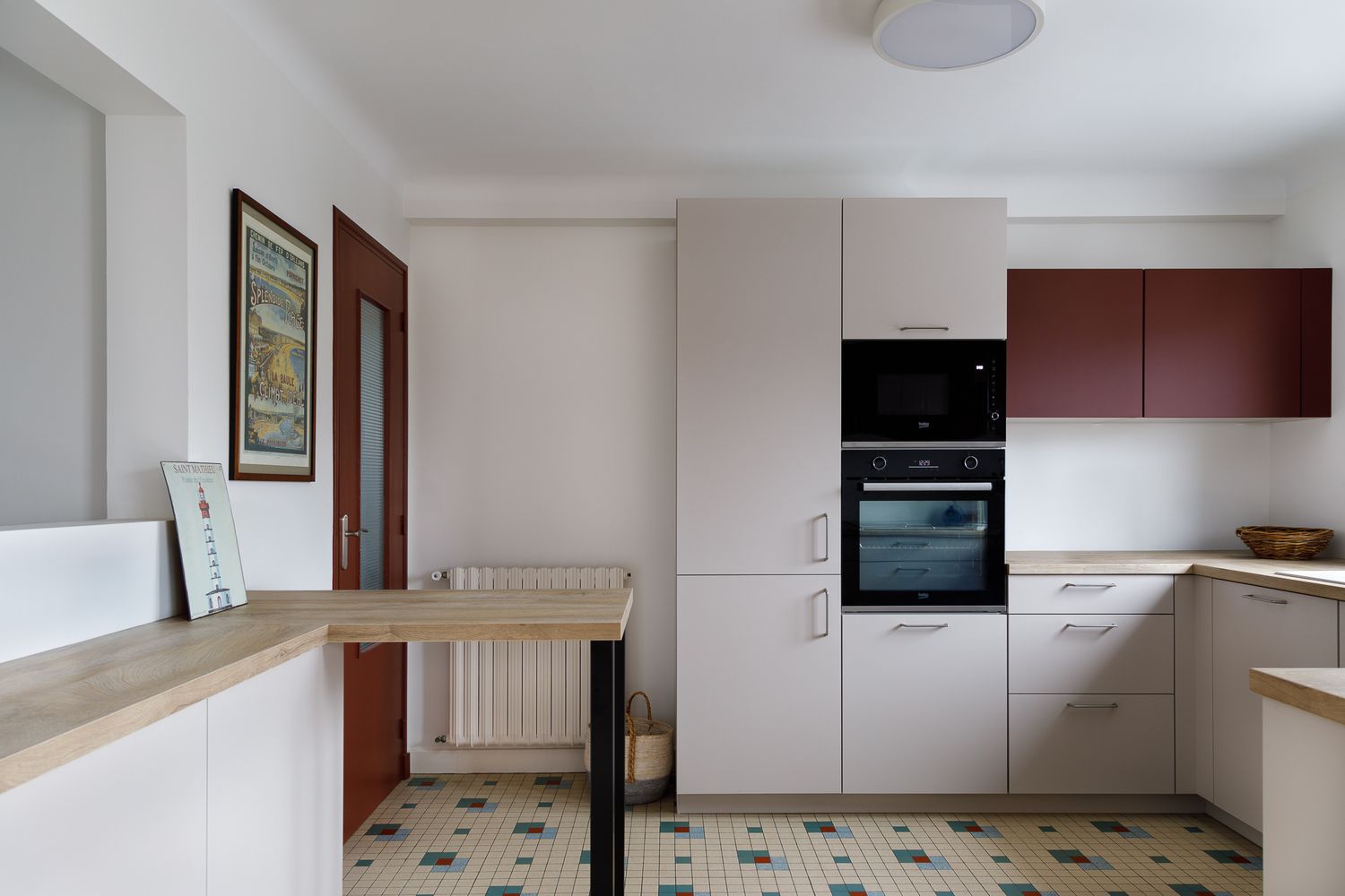 Cuisine contemporaine avec des placards bordeaux et beiges, un four encastré, un plan de travail en bois et un sol carrelé coloré.
