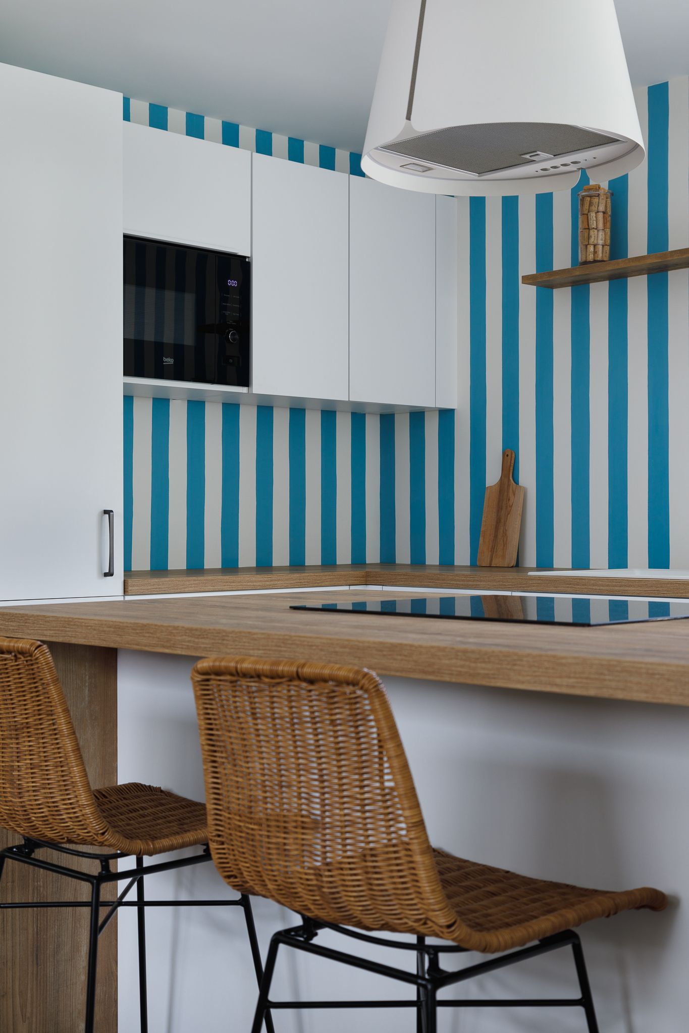 Cuisine moderne avec un mur d'accent rayé bleu et blanc, des placards blancs, un îlot à plan de travail en bois et des tabourets de bar