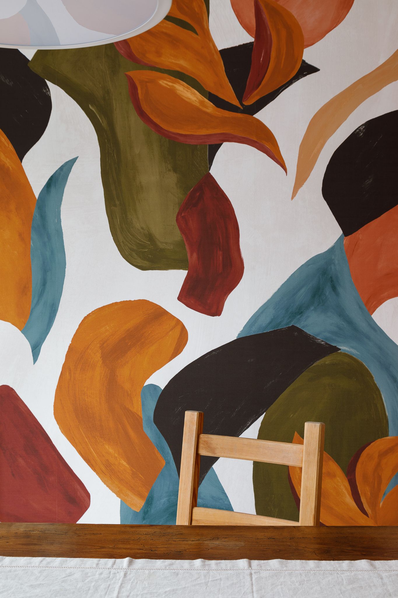 Fresque murale abstraite et colorée aux formes organiques dans des tons orange, vert, bleu sarcelle et marron, située derrière une chaise
