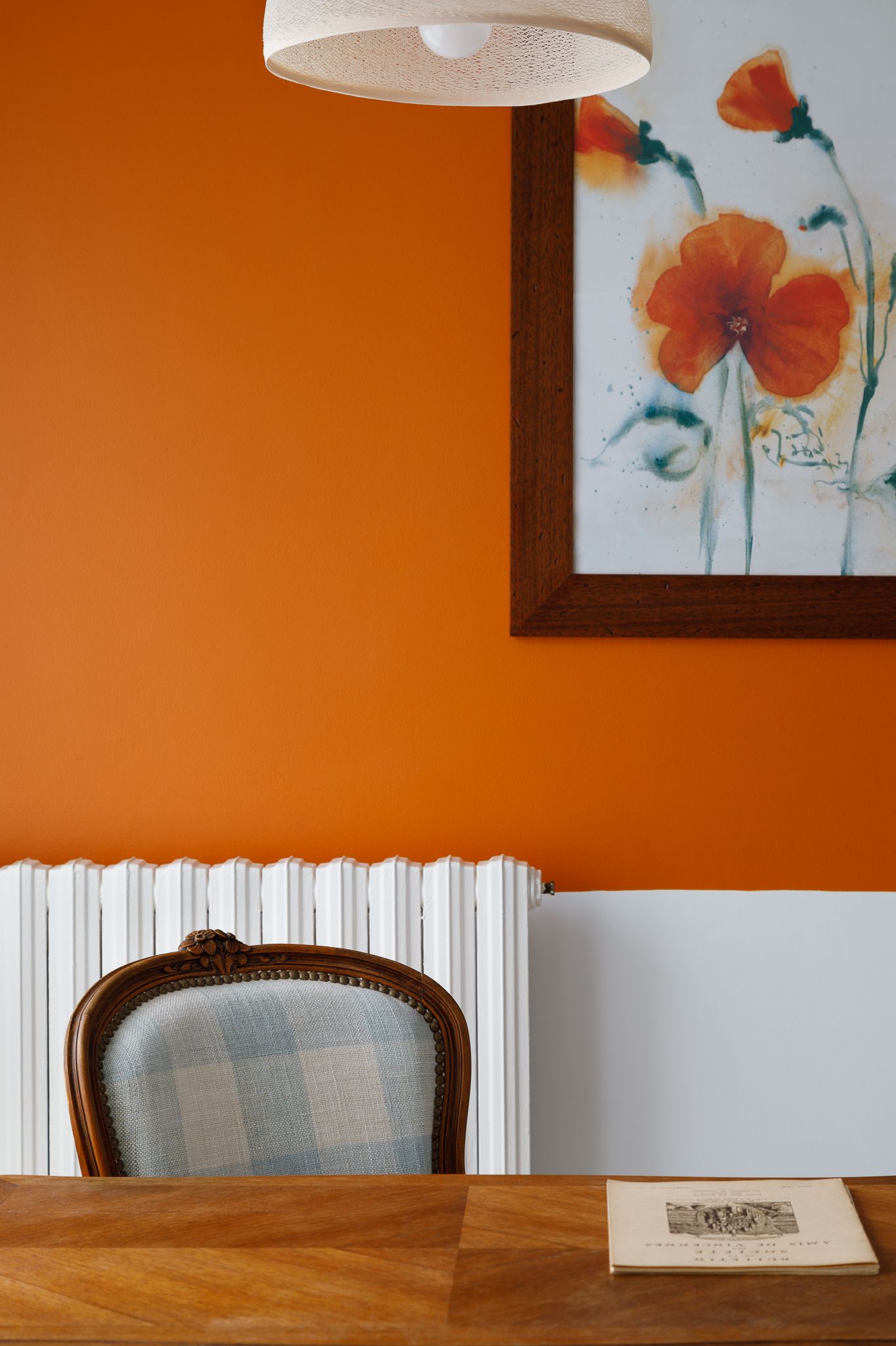 Mur de salle à manger d'un orange éclatant avec une œuvre d'art florale, une chaise classique rembourrée, un radiateur blanc