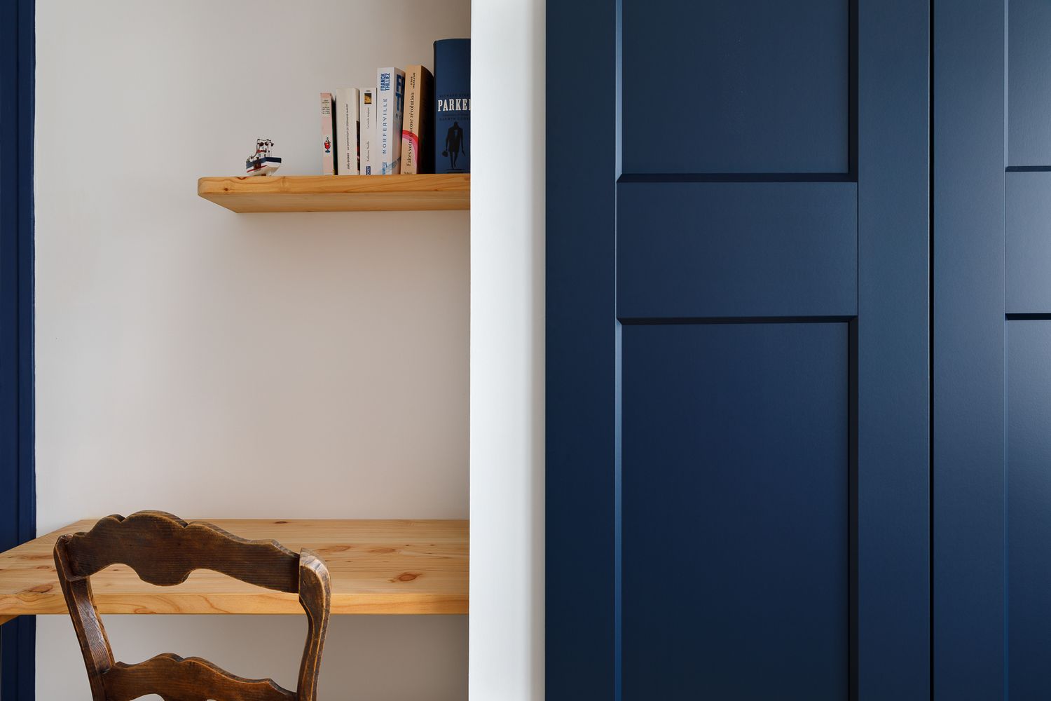 Coin bureau chaleureux avec une étagère murale en bois, des livres et une porte à panneaux d'un bleu marine audacieux au premier plan.