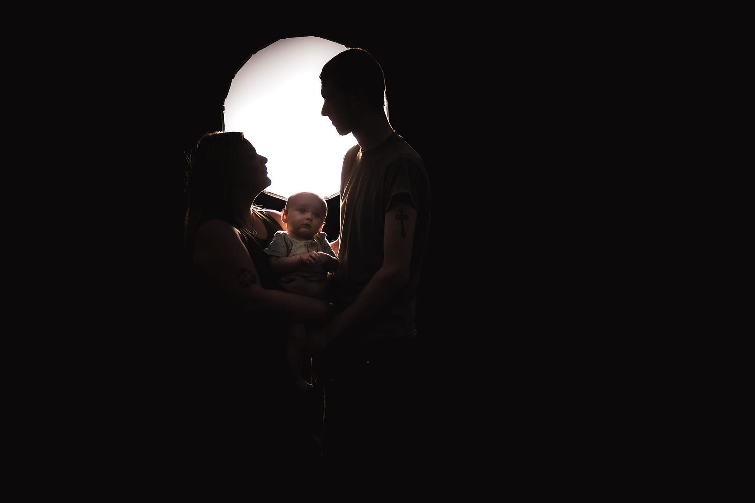Silhouetted family with baby illuminated by circular backlight in dark setting.