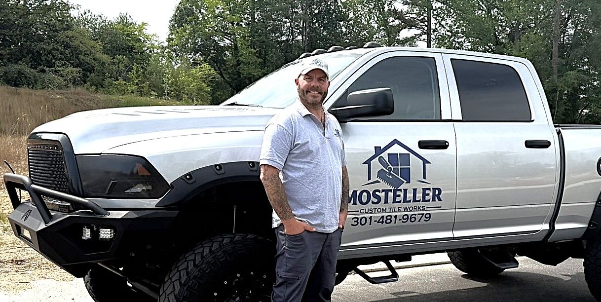 Mosteller contractor standing beside white lifted Ram work truck on a dirt road outdoors.