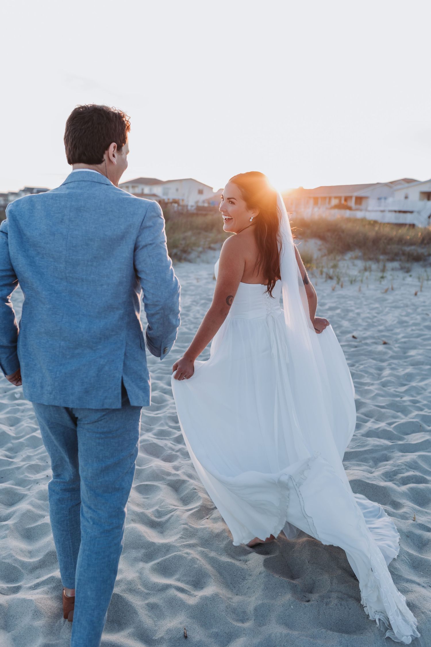 Bride and groom kissing under an arch at sunset, dramatic orange sky backdrop, elegant wedding venue balcony.