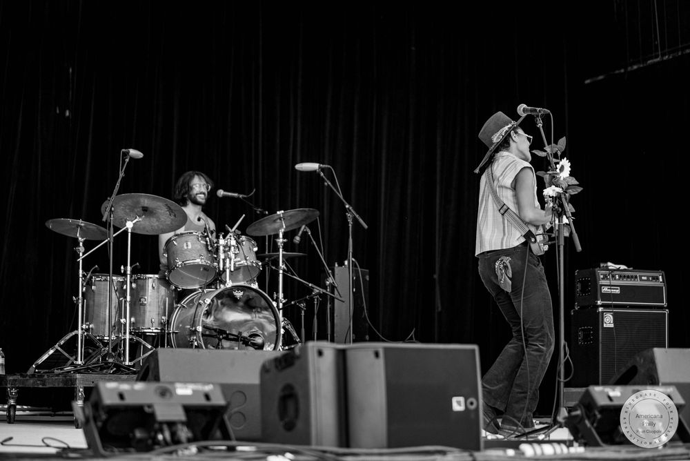 Black and white photo of a live band performance with a drummer and guitarist on stage.