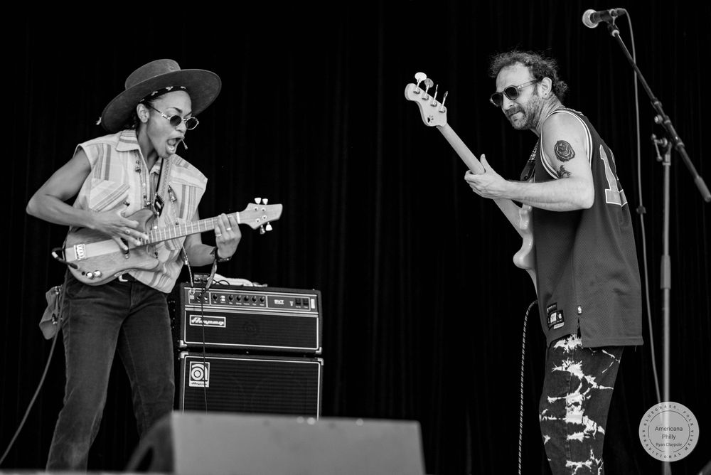Two musicians playing electric guitars on stage in black and white photo at outdoor concert.
