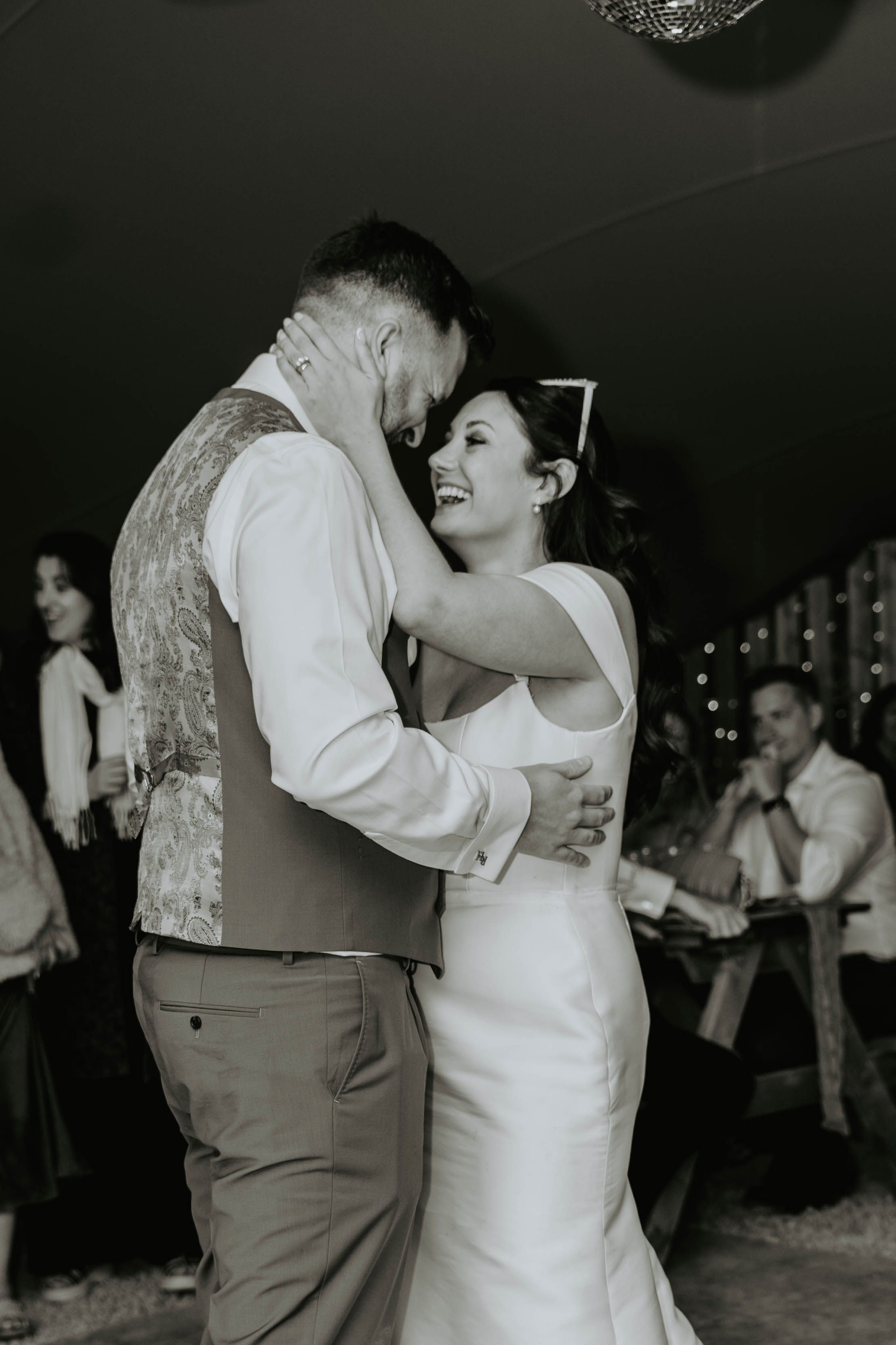 A bride and groom share an emotional first dance, laughing together in a tender black and white wedding photo.