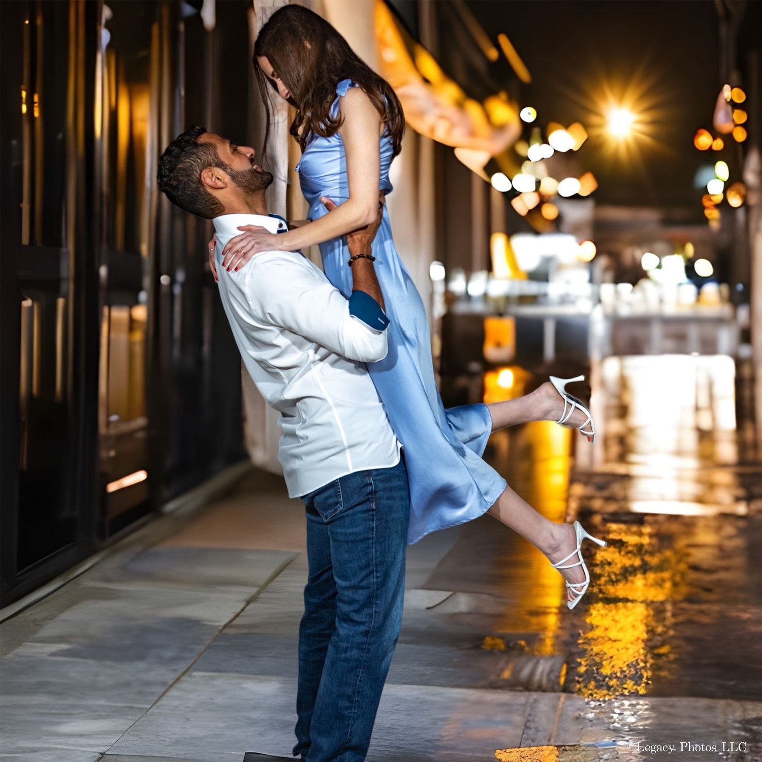 Couple laughing and dancing together at an evening engagement session with warm city lights.