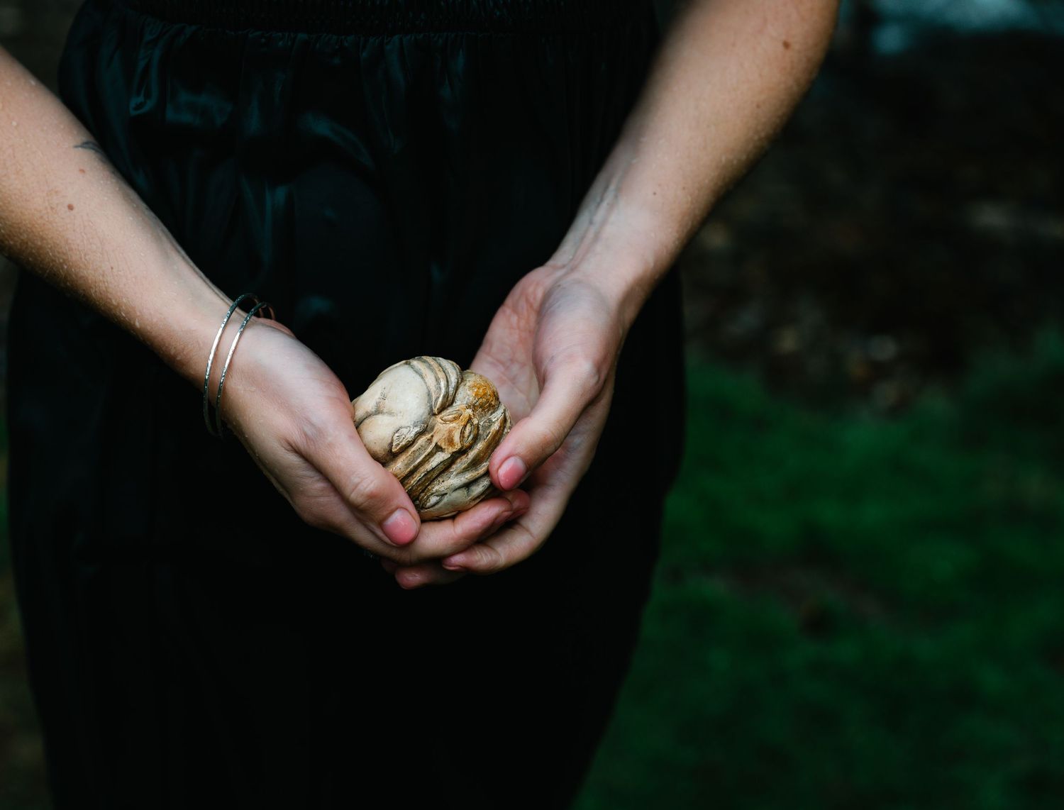 Person in black dress holding a handful of small mushrooms in cupped hands outdoors.