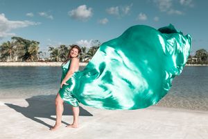 An emerald green flowing dress creates dramatic movement against a beachfront setting.