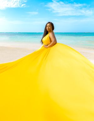 Vibrant yellow flowing dress creates dramatic movement against turquoise ocean and white sand beach.