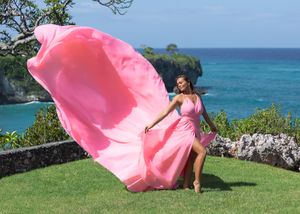 A pink flowing dress catches the breeze on a scenic clifftop overlooking turquoise waters.