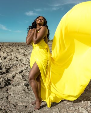 A bright yellow dress flows dramatically against a desert landscape under blue skies.